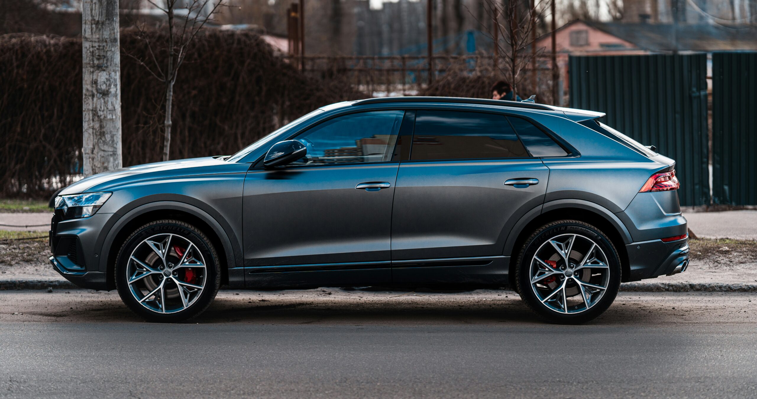 A modern SUV parked on a street, featuring a sleek gray body and distinctive red brake calipers visible through diamond-cut alloy wheels.